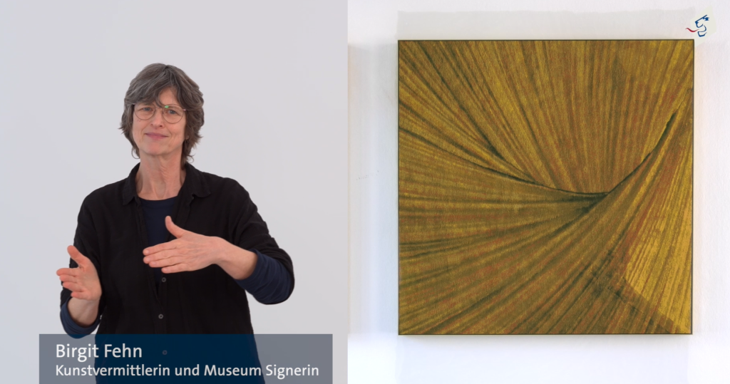 Die Kustvermittlerin und Museum Signerin Birgit Fehn steht links und gebärdet über ein Kunstwerk, das rechts von ihr eingeblendet wird. Im oberen rechten Rand ist das Logo des Bezirks Oberbayern zu sehen. 